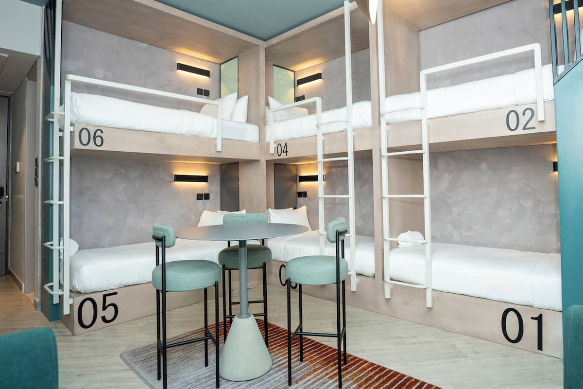 A bunk room with three bunk beds, a round table with chairs, and a number on each bed.