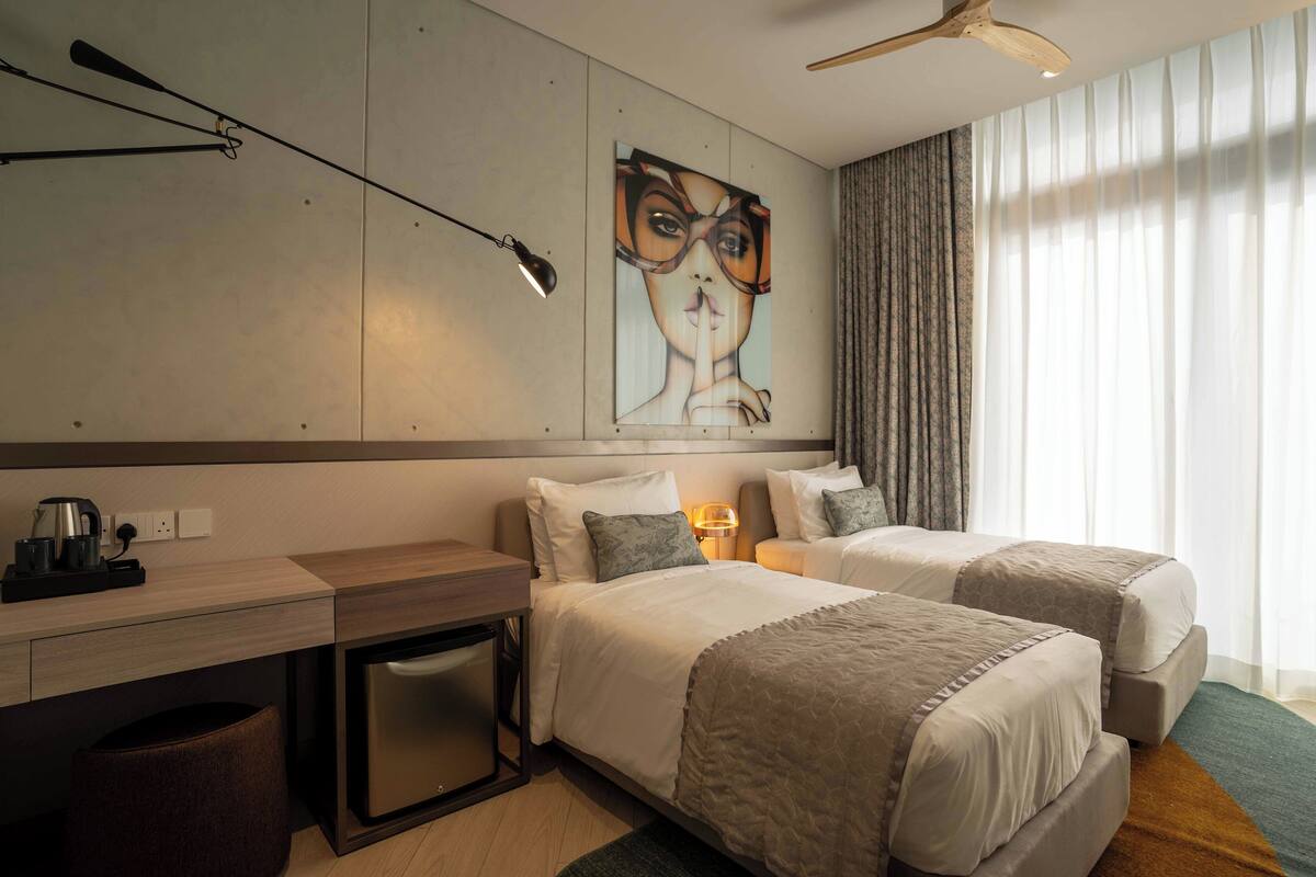A hotel room with two beds, a desk, a coffee maker, and a painting on the wall.