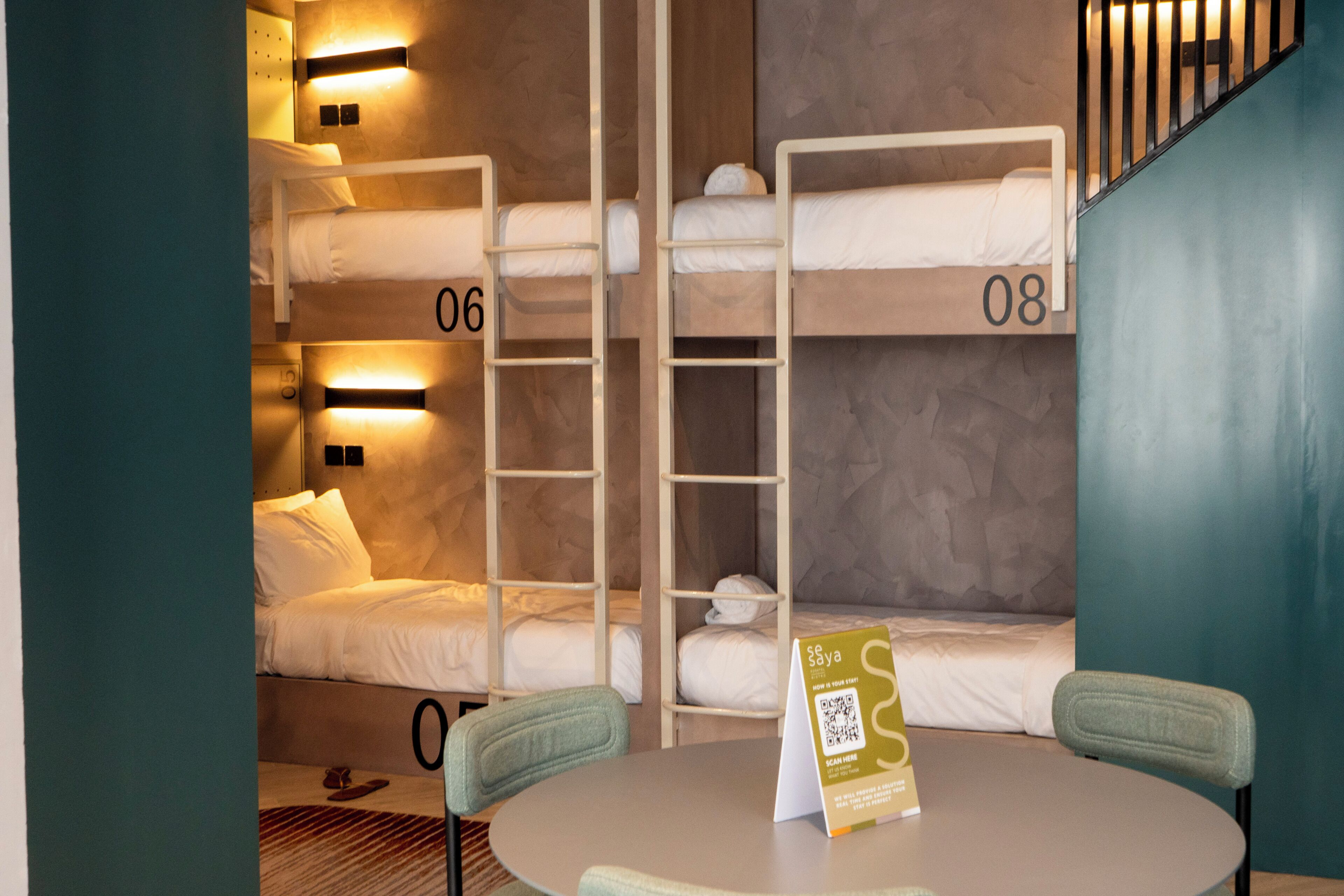 Una habitación de hotel con literas, una mesa redonda y un cartel con un código QR.