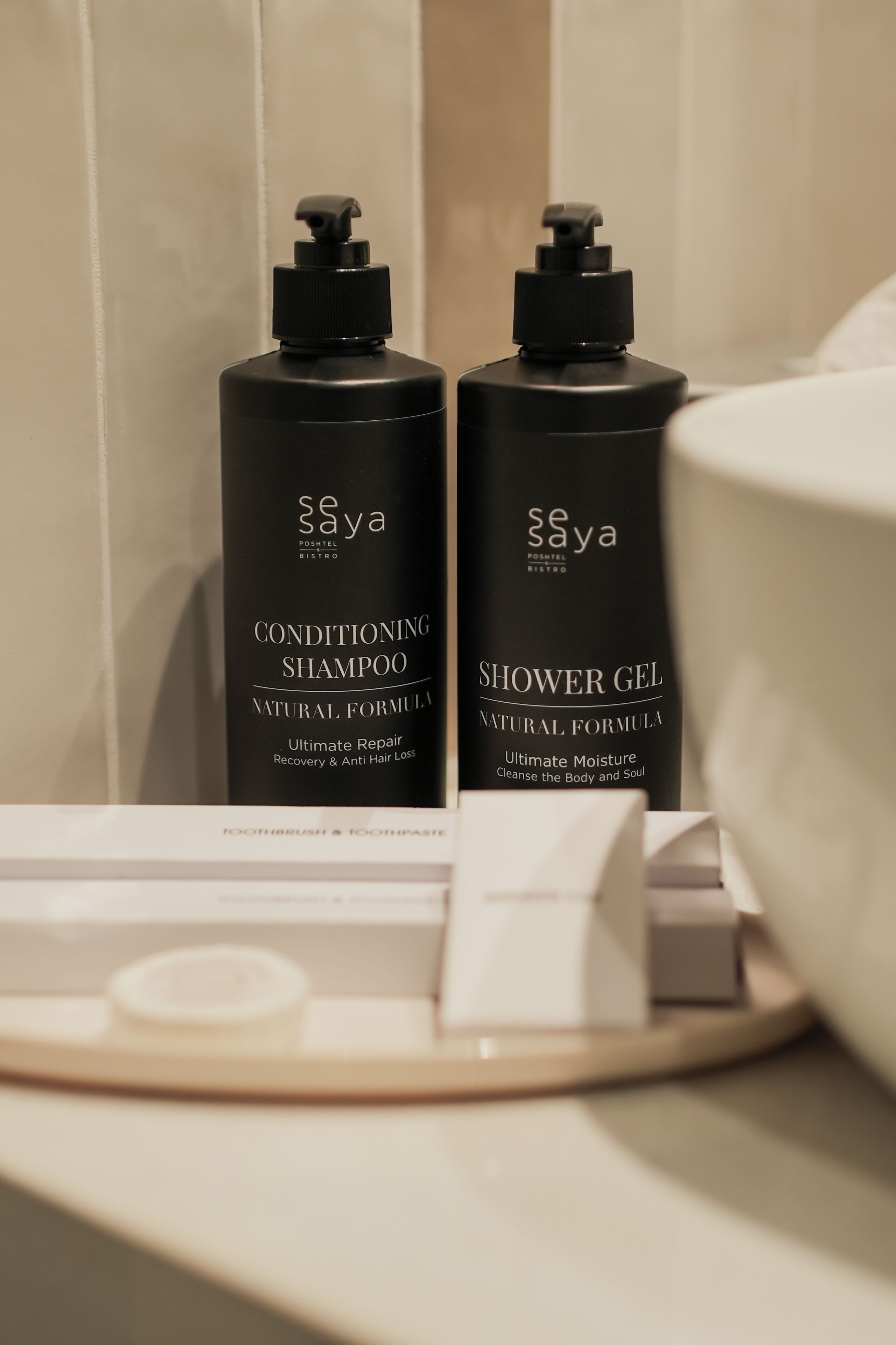 Two black bottles of Soya conditioning shampoo and shower gel on a bathroom counter.