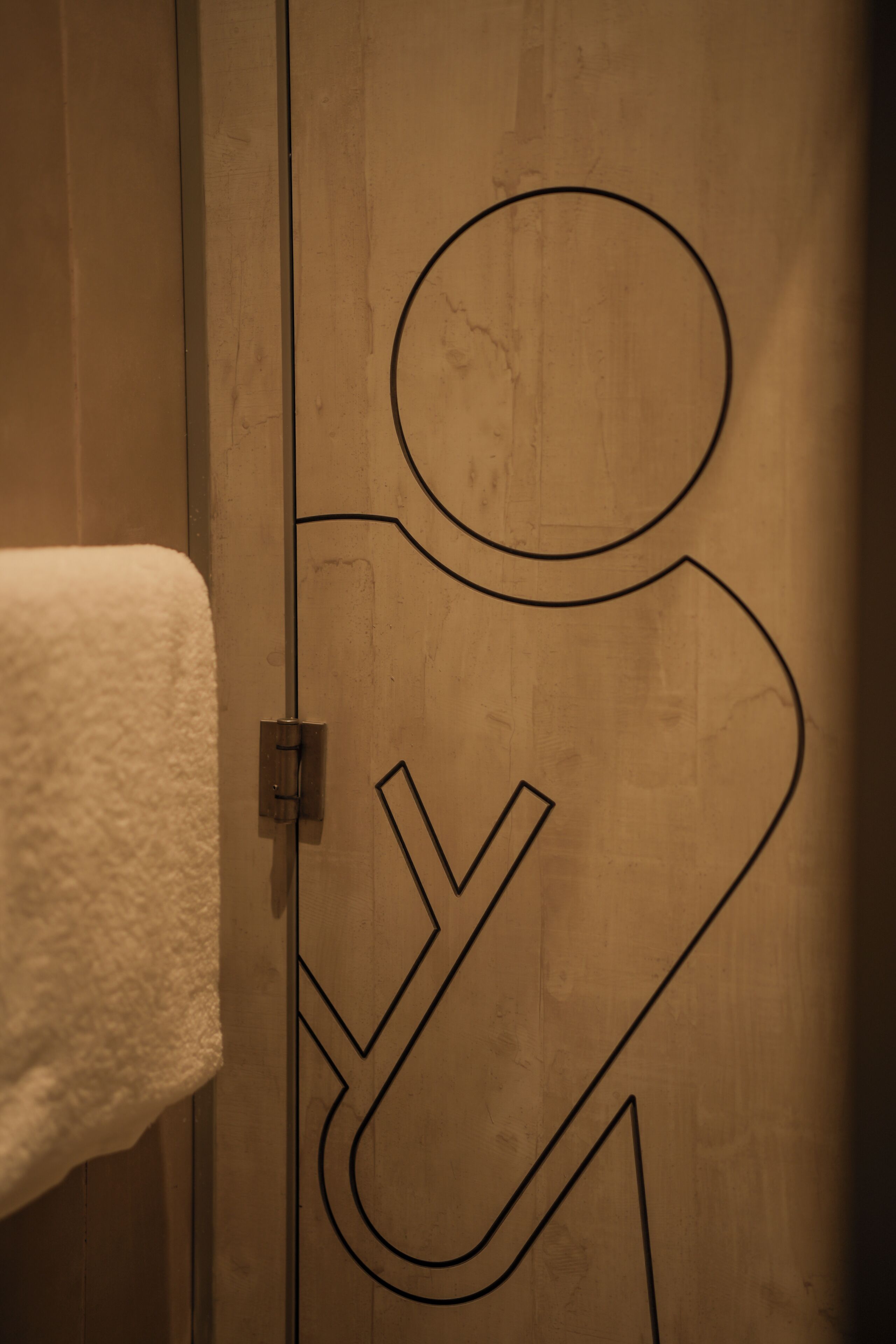 A wooden door with a simple line drawing of a person, a towel hanging on the left, and a door handle.