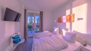 Ein modernes Schlafzimmer mit Bett, Sessel, Fernseher und Blick ins Freie.