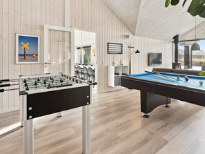 A room with a foosball table, a pool table, and a dining area with chairs and a table.