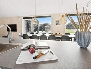 A modern kitchen with a built-in sink, a cutting board with a knife and onion, and a vase with dried plants. - 5 Star Holiday Home in Romo (Rømø)