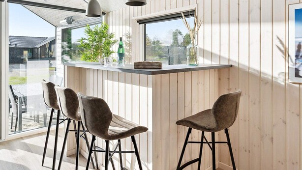 A modern kitchen with a bar area, wooden paneling, and a view of the outdoors. - 5 Star Holiday Home in Romo (Rømø)