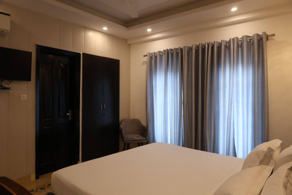 A hotel room with a bed, a chair, a wardrobe, and a curtain.