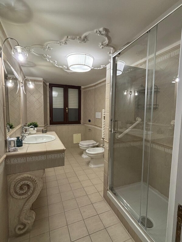 A bathroom with a large mirror, a sink, a toilet, and a glass-enclosed shower. - Dimora71 (Naples)