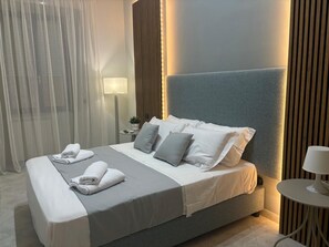 A modern hotel room with a large bed, grey bedding, and a bedside table with a lamp. - Dimora71  (Naples)