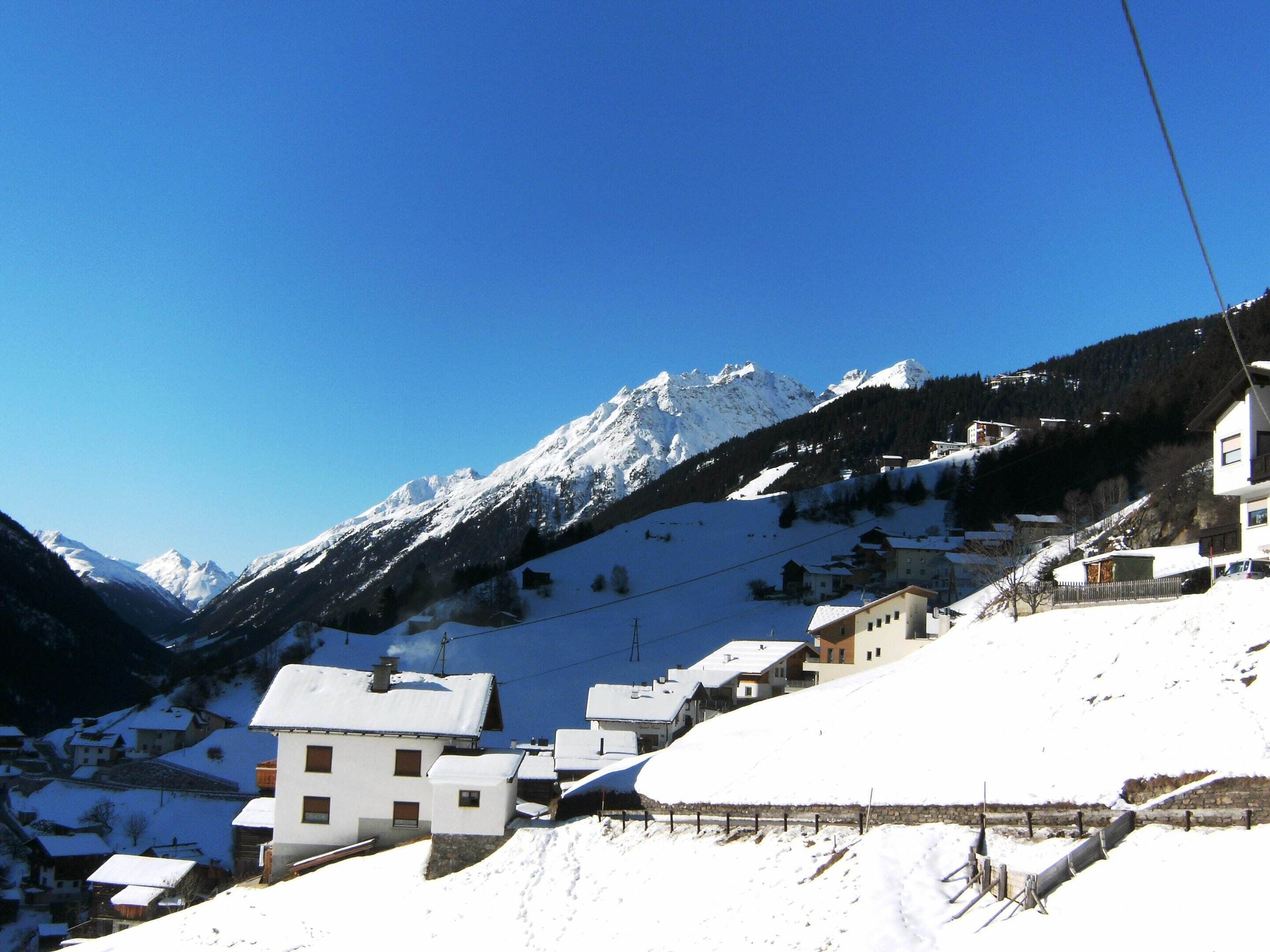 Ein verschneites Bergdorf mit Häusern, einer Seilbahn und blauem Himmel.