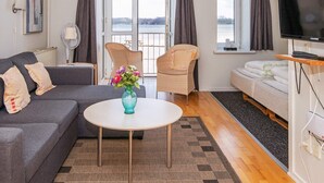 A modern living room with a sofa, armchairs, a small round table with a vase, a TV, and a balcony with curtains. - 4 Person Holiday Home on a Holiday Park in Hejls (Hejls)