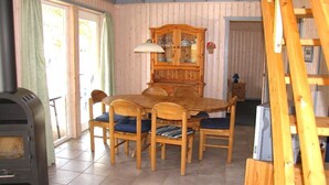 Een eethoek met een houten tafel en stoelen, een inbouwkast en een houtkachel.