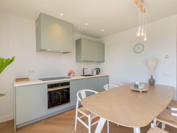 A modern kitchen with a central island, white chairs, and a wooden dining table. - Nice Countryside Home With Garden (Zoutelande)