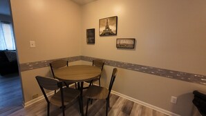 Un comedor con una mesa redonda y cuatro sillas, una pared decorativa con un borde de azulejos y dos cuadros con imágenes de la Torre Eiffel.