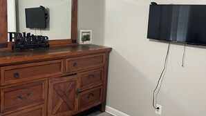 Una habitación con un aparador de madera, un televisor de pantalla plana montado en la pared y un pequeño cuadro en el aparador.