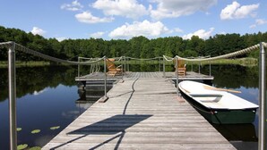 Une jetée en bois s’étendant sur une étendue d’eau calme, avec une barque à rames et des chaises longues.
