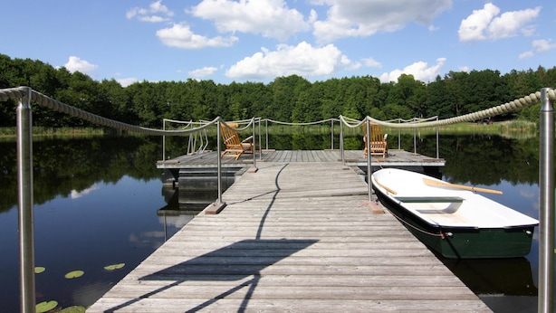A wooden dock extending into calm water with a rowboat and lounge chairs. - Ferienhaus Birgit, Wendorf (Kuhlen-Wendorf)