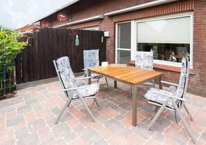 Relax on the patio with a wooden table and comfortable chairs, surrounded by a brick wall and a wooden fence.