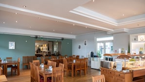 A spacious dining area with wooden tables and chairs, a kitchen in the background, and a view of the city through large windows. - Elegant Eingerichtete Ferienwohnung (Mirow)