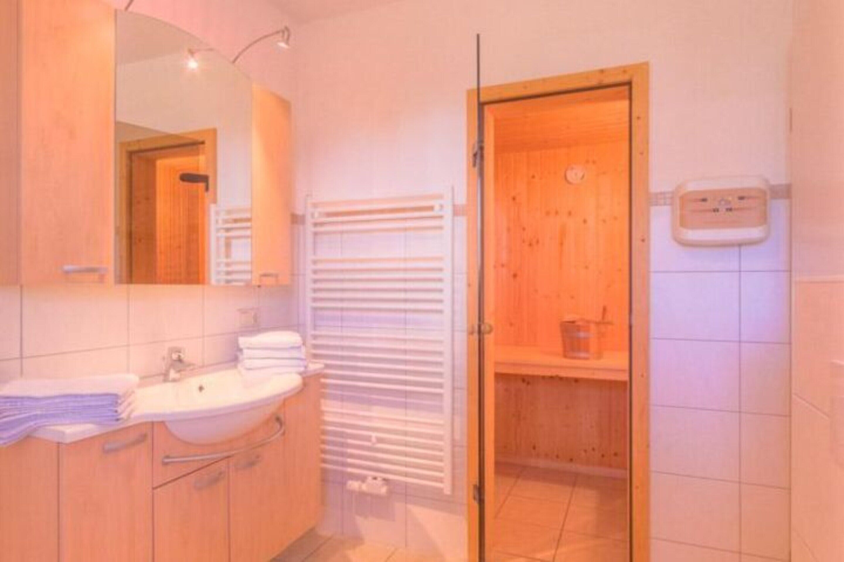 A bathroom with a wooden vanity, a sink, a mirror, a towel rack, and a shower area with a wooden door.
