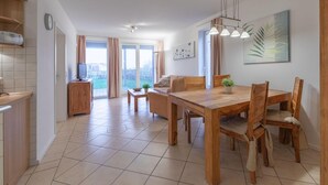 A modern kitchen with a built-in oven, a dining area with a wooden table and chairs, and a view of the outdoors through large windows. - Tolles Appartment in der Seenplatte (Rechlin)