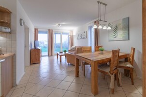 A modern kitchen with a built-in oven, a dining area with a wooden table and chairs, and a view of the outdoors through large windows.