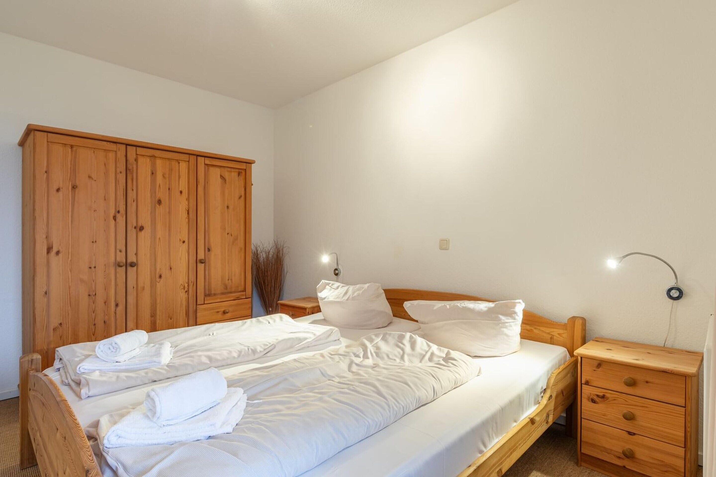 Un dormitorio con cama de madera, ropa de cama blanca, un armario de madera y lámparas de noche.