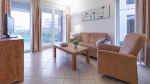 A modern living room with a wooden coffee table, a sofa, and a chair. There is a television on a wooden cabinet, and a potted plant on the table. - Tolles Appartment in der Seenplatte (Rechlin)