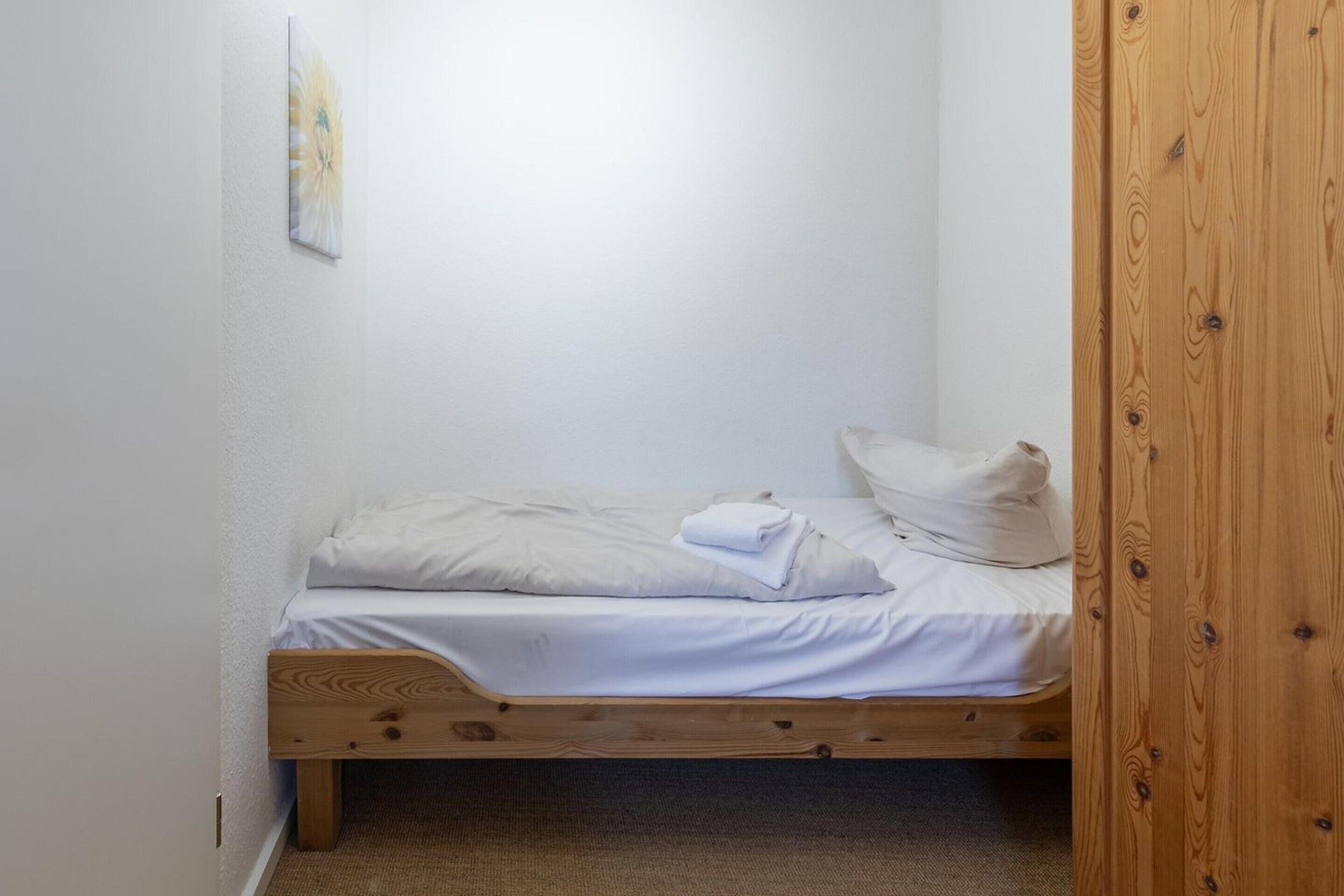A small, single-bed room with a wooden frame, white bedding, and a small wooden nightstand.