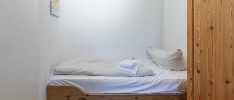 A small, single-bed room with a wooden frame, white bedding, and a small wooden nightstand.