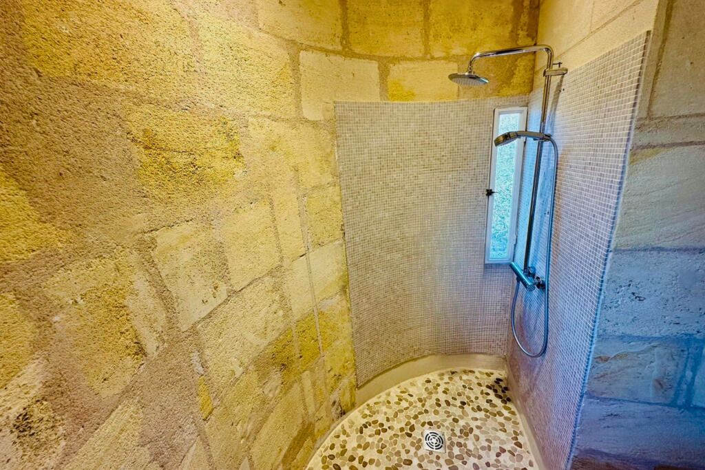 A stone-walled shower with a textured floor, a showerhead, and a small window.
