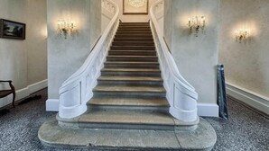 A grand staircase with a chandelier at the top, flanked by wall sconces. - Château du XIVe - privatization 15 travelers, salt pool, Bordeaux 25 min (St-Sulpice & Cameyrac, 33450)