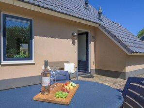 A table with a bottle of wine, glasses, and a fruit platter outside a building with a tiled roof and a window. - Bungalow in Sondel Near Slotermeer Lake (Sondel)