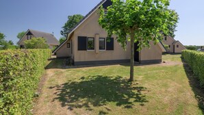 A single-story house with a sloped roof, a small front porch, and a tree in the front yard. - Bungalow in Sondel Near Slotermeer Lake (Sondel)