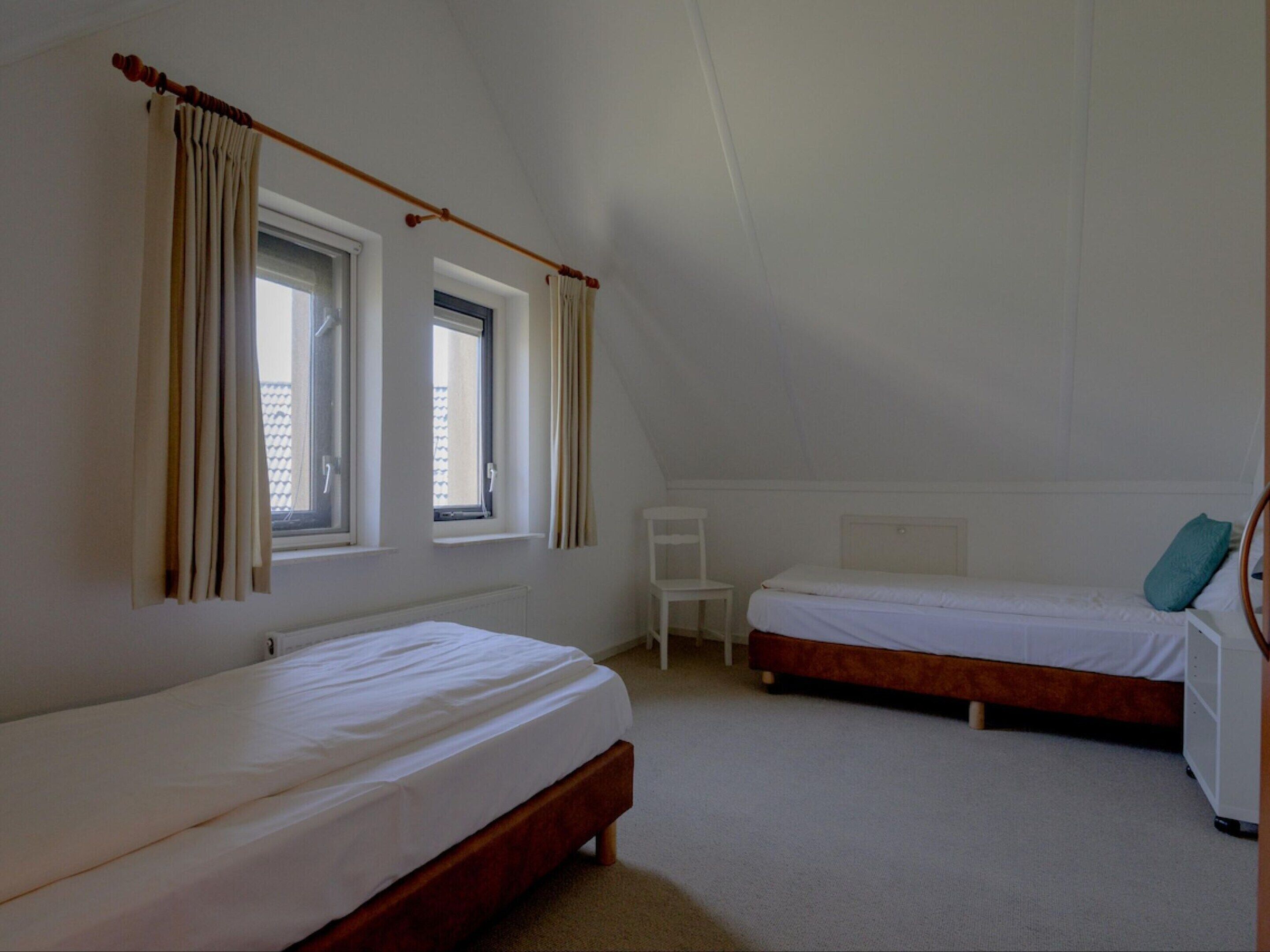 A bedroom with two beds, a chair, and a radiator.