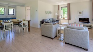 A spacious living area with a sofa, a coffee table, and a TV. There is a dining area with a table and chairs. - Bungalow in Sondel Near Slotermeer Lake (Sondel)