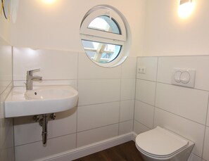 Un baño con un lavabo blanco, una ventana redonda y un inodoro.