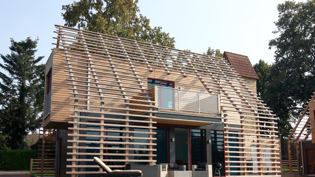 Una casa moderna con facciata in legno, ampie finestre e un balcone con mobili da esterno.