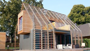 Una casa moderna con tetto spiovente, rivestimento in legno e un balcone con ringhiera in metallo.