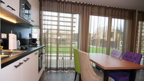 Una cucina moderna con zona pranzo, caratterizzata da un tavolo e sedie in legno, un'ampia finestra con tende e vista sull'esterno.