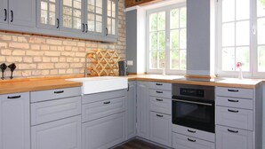 A kitchen with grey cabinets, a wooden countertop, a brick backsplash, and a large window with a view of greenery. - Ferienhaus Birgit, Wendorf (Kuhlen-Wendorf)