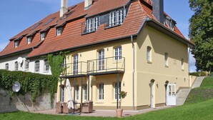 A large, yellow building with a red-tiled roof, multiple chimneys, and a balcony with outdoor furniture. - Ferienhaus Birgit, Wendorf (Kuhlen-Wendorf)