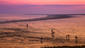 Àmplia platja al capvespre amb gent caminant i jugant a la sorra.