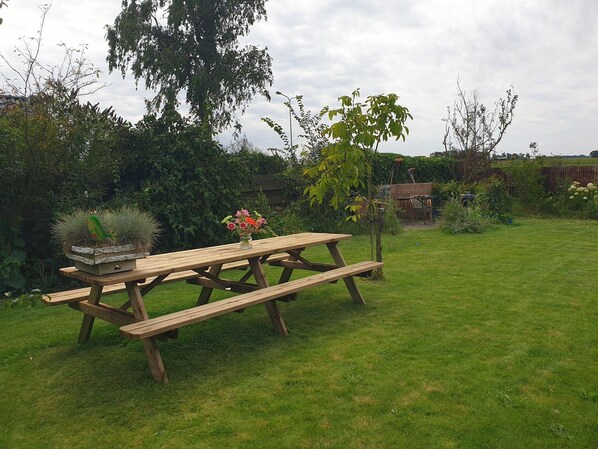 A wooden picnic table in a grassy backyard with a vase of flowers and a birdhouse. - Famous Historic Inn Near Heritage Site (Ternaard)