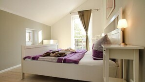 A bedroom with a single bed, a window with curtains, a bedside table with a lamp, and a view of the outdoors.