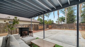 Ein überdachter Patio-Bereich mit einer Couch, einem Holztisch und einer kleinen Bar.