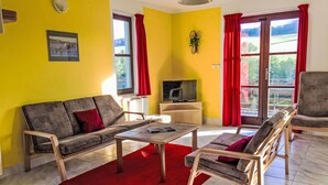 Un salon avec un canapé, des fauteuils, une table basse, un téléviseur et un tapis rouge.
