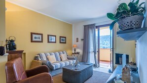 Un salón con un sofá, un sillón y una mesita con una lámpara. Hay cuadros enmarcados en la pared y una planta en una estantería.