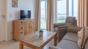 Ein Wohnzimmer mit einem Holz-TV-Schrank, einer Couch, einem Couchtisch und Blick ins Freie durch große Fenster.