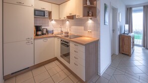 Eine moderne Küche mit weißen Schränken, einer Mikrowelle, einem Herd und einem Spülbecken. Ein Holzkasten mit Ablagefläche befindet sich über dem Spülbecken.