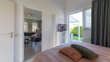 A bedroom with a bed, a television, and a view of a balcony.